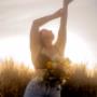 woman with flowers in jeans with arms up against the sunset